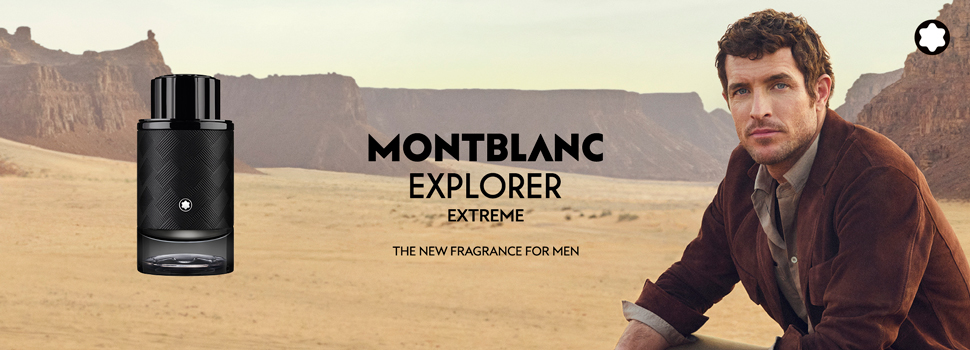 Werbung für Montblanc Explorer Extreme Herrenduft. Links im Bild eine schwarze Parfümflasche mit Montblanc-Logo. Im Hintergrund eine weite, trockene Wüstenlandschaft mit Tafelbergen. Rechts sitzt ein Mann mit lockigem Haar in brauner Jacke und grauem Hemd, der in die Kamera blickt. Text in der Mitte: 'Montblanc Explorer Extreme – The New Fragrance for Men'.