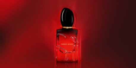 Rotes Parfumflakon des Dufts 'Giorgio Armani Sì' auf rotem Hintergrund. Die Flasche ist durchsichtig mit goldfarbenem Schriftzug 'Giorgio Armani' und schwarzem Verschluss. Der Hintergrund ist in dunklen und hellen Rottönen gehalten, die das Parfum dramatisch hervorheben.