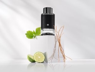 Montblanc Explorer Eau de Parfum in einem schwarz-silbernen Flakon. Der Flakon steht auf einem weißen Podest, daneben frische grüne Blätter, Limettenscheiben und trockene Wurzeln – symbolisch für die enthaltenen Duftnoten.